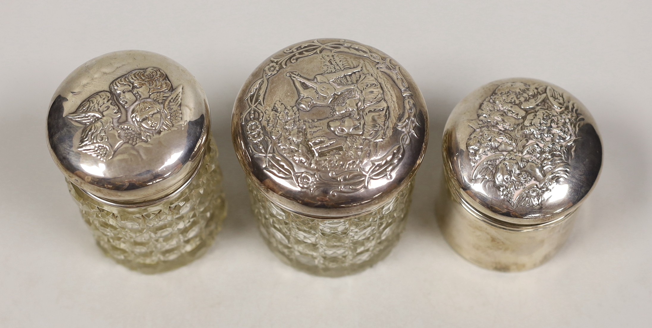Two early 20th century silver mounted glass Reynolds angel lid toilet jars, tallest 89mm and one other silver mounted toilet jar.